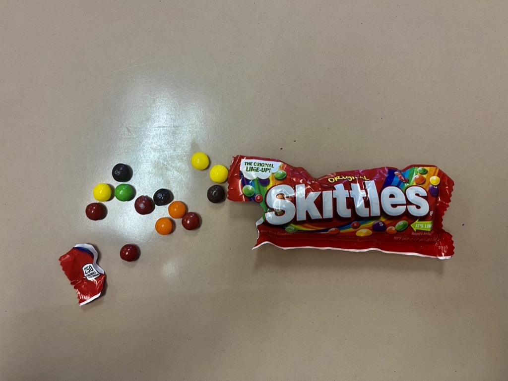 A rainbow of Skittles pours out of a Skittles bag