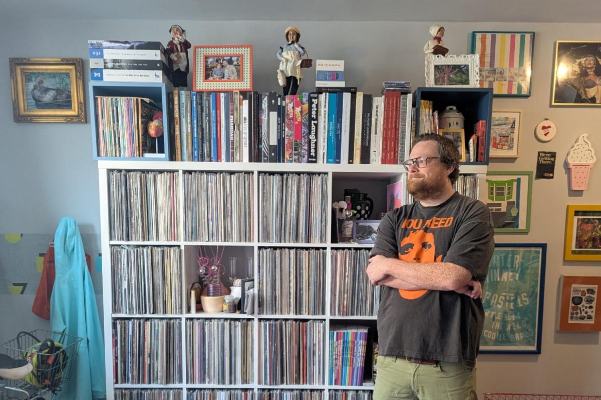 Kevin Gary ‘02 posing next to a centerpiece of his record collection inside his living room.