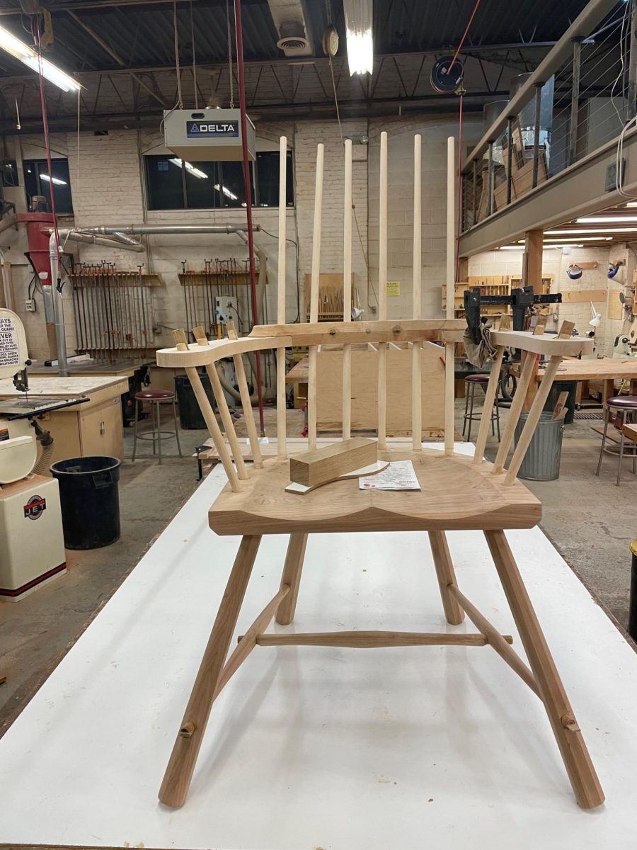 A finely crafted chair halfway built  sitting on display in a busy woodshop 